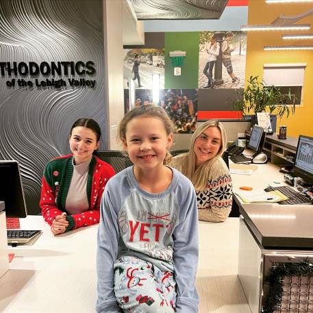 Two team members at the front desk with young girl wearing Christmas outfits